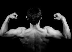 Black and white photo of a muscular man flexing arms against a dark background.