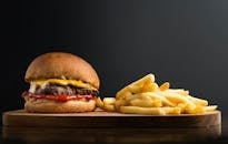 Appetizing burger with meat patty ketchup and cheese placed on wooden table with crispy french fries against black background