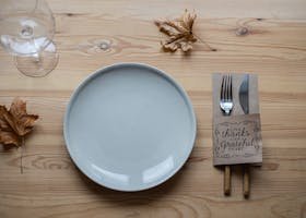 Elegant Thanksgiving table setting with plate, utensils, and autumn leaves on wooden surface.