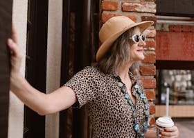 A fashionable senior woman in leopard print and sunglasses holding coffee in a vibrant city setting.
